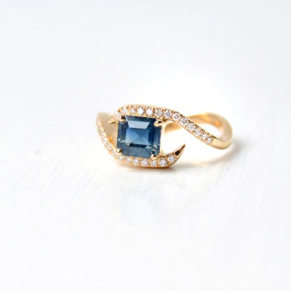emerald cut teal sapphire ring with diamonds set in 18K yellow gold.