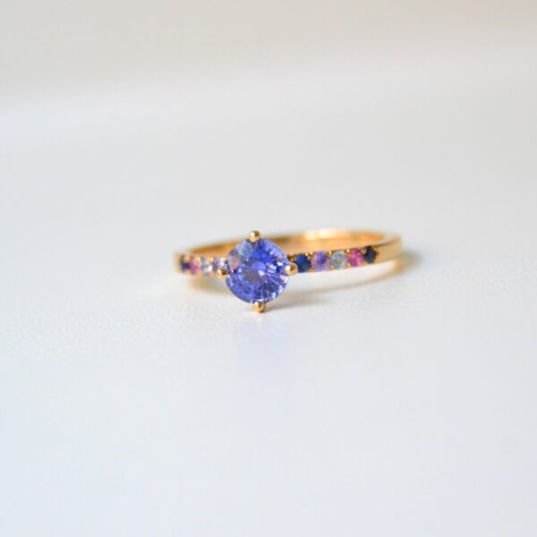 Blue sapphire ring with a splash if rainbow sapphires in the band of 18k yellow gold
